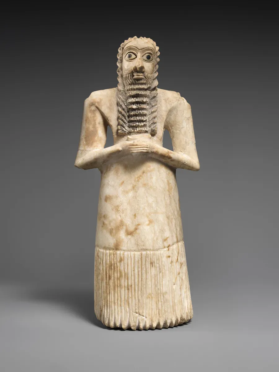 Small standing stone figure of a man with clasped hands, a long beard and huge inlaid eyes