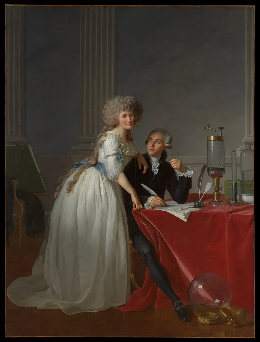 A woman in white leans on her husband, who sits writing beside glass laboratory instruments
