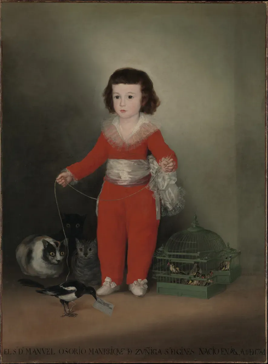 A small boy in a red suit holds a magpie on a string while cats stare at it from the shadows