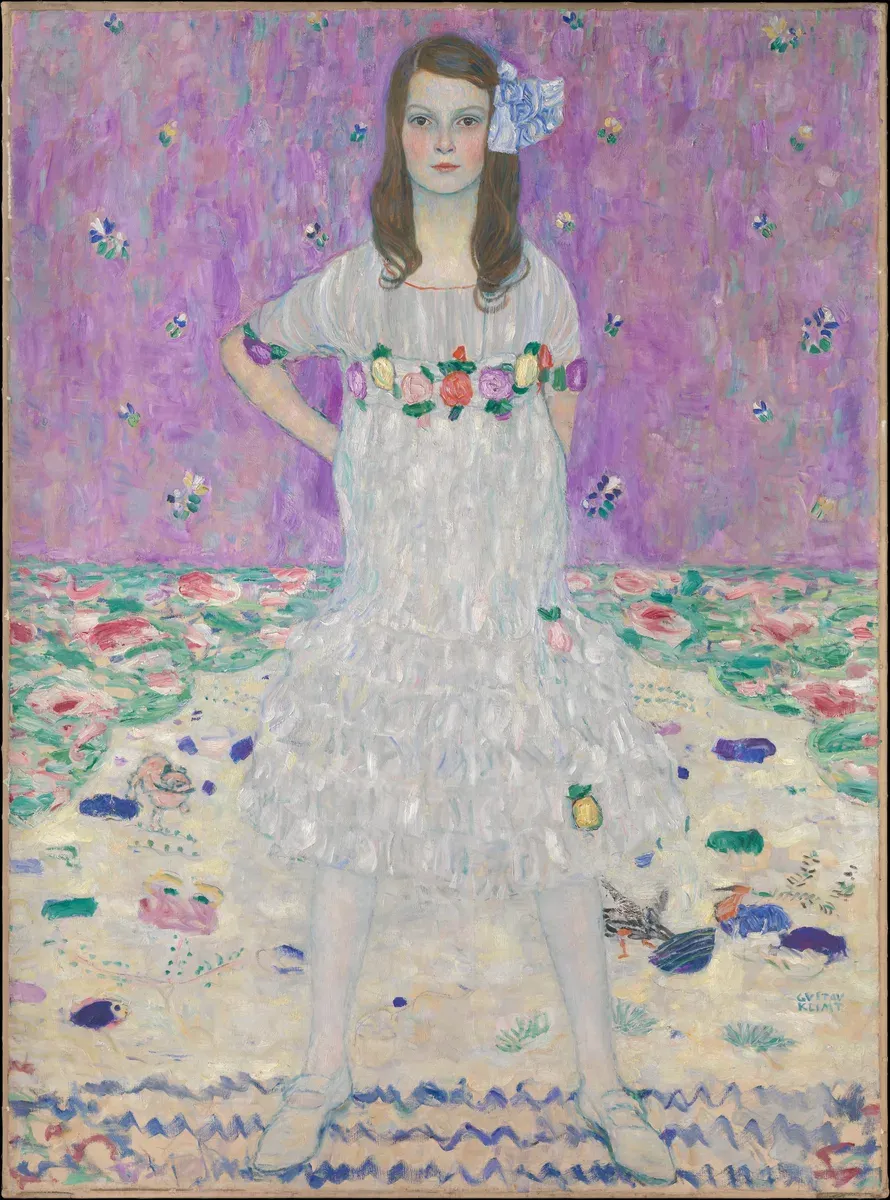 A young girl in a white dress stands with legs apart before a pale flowered background