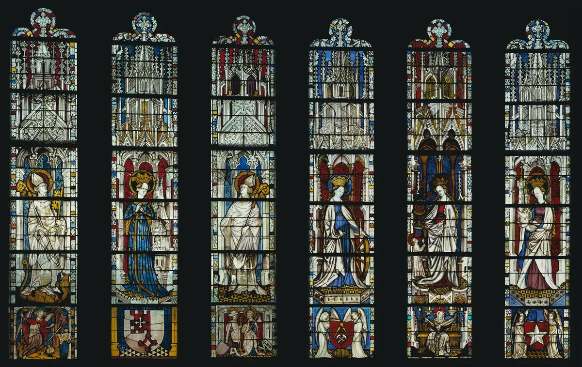 Stained glass windows with the Virgin Mary and saints standing under tall painted canopies above small scenes