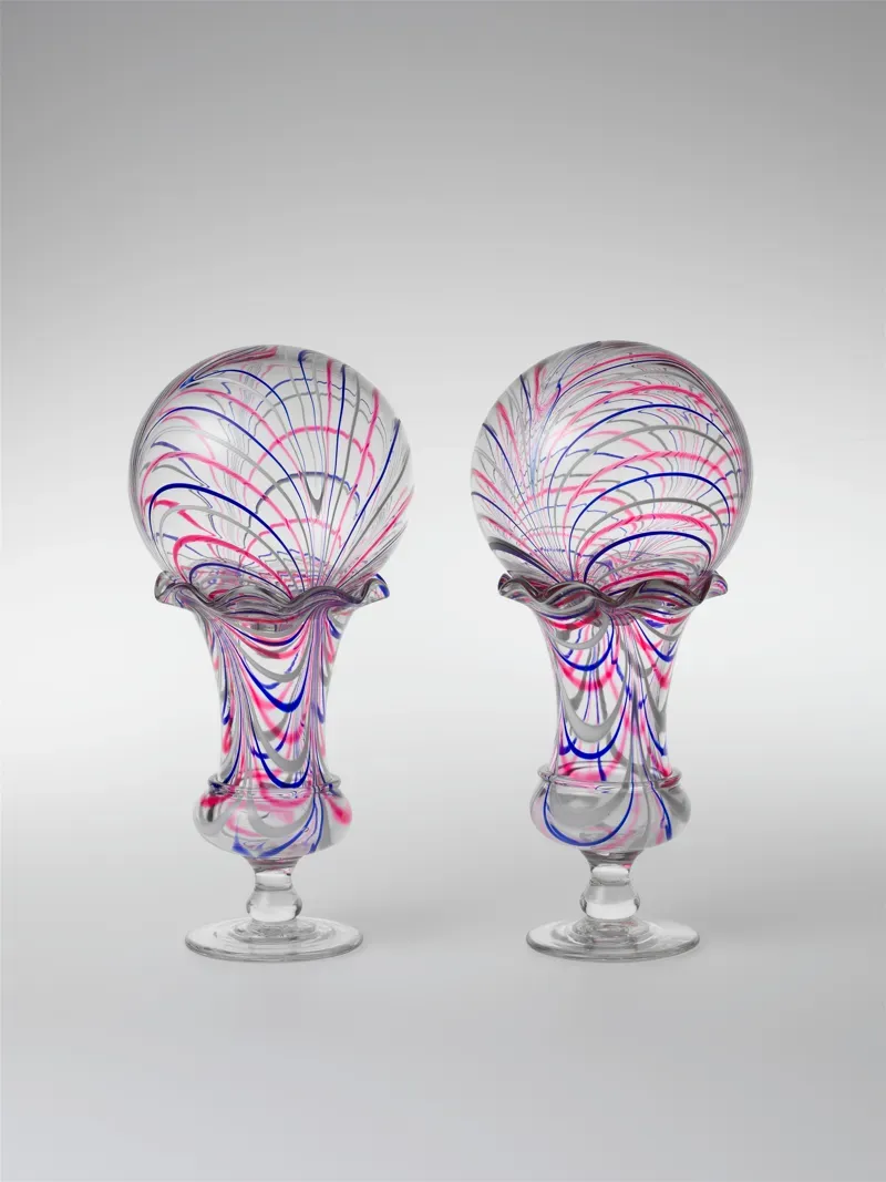 Two clear glass vases, each holding a round glass ball swirled with pink, blue and white stripes